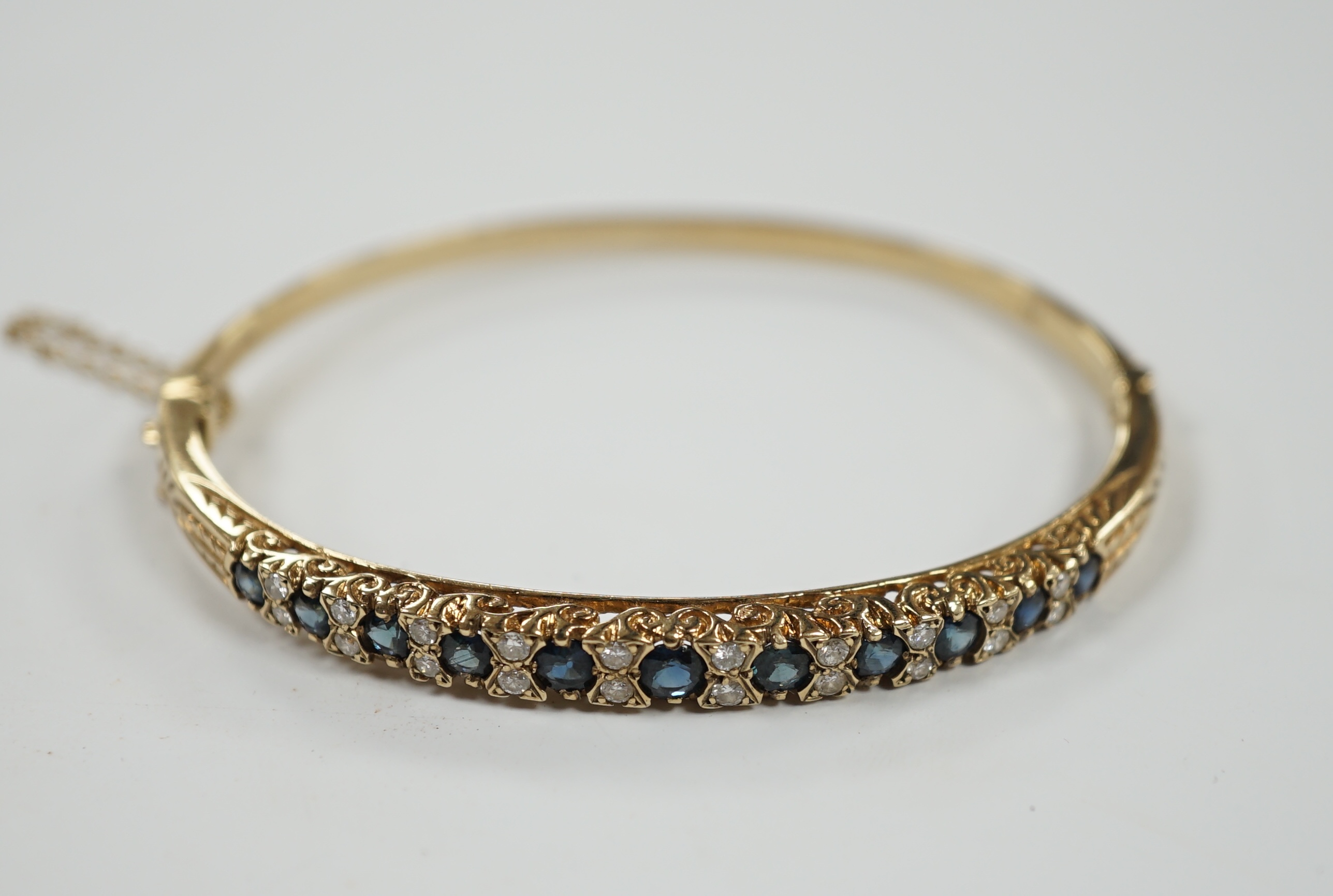 A modern 9ct gold, sapphire and diamond cluster set hinged bangle, gross weight 14 grams.